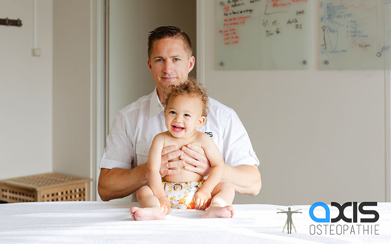 Samuel houdt baby vast rond middenrif op behandeltafel