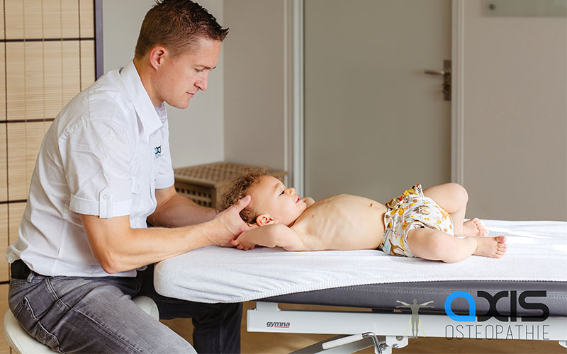 Samuel ondersteunt baby bij achterhoofd op behandeltafel